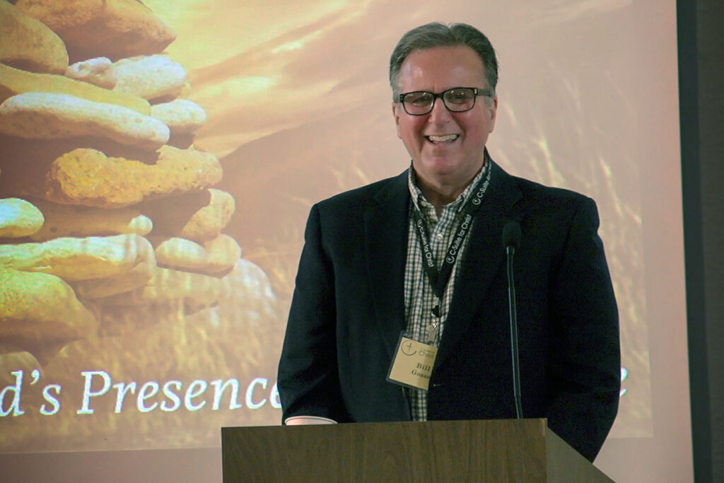Bill Gosse smiling during a speaking event, standing in front of a presentation screen